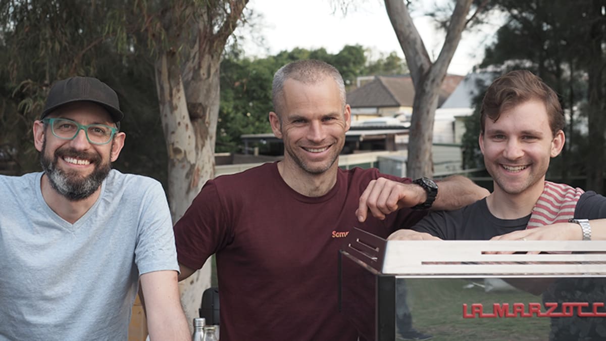 A photo of Simon, Reuben and John K behind the coffee machine.