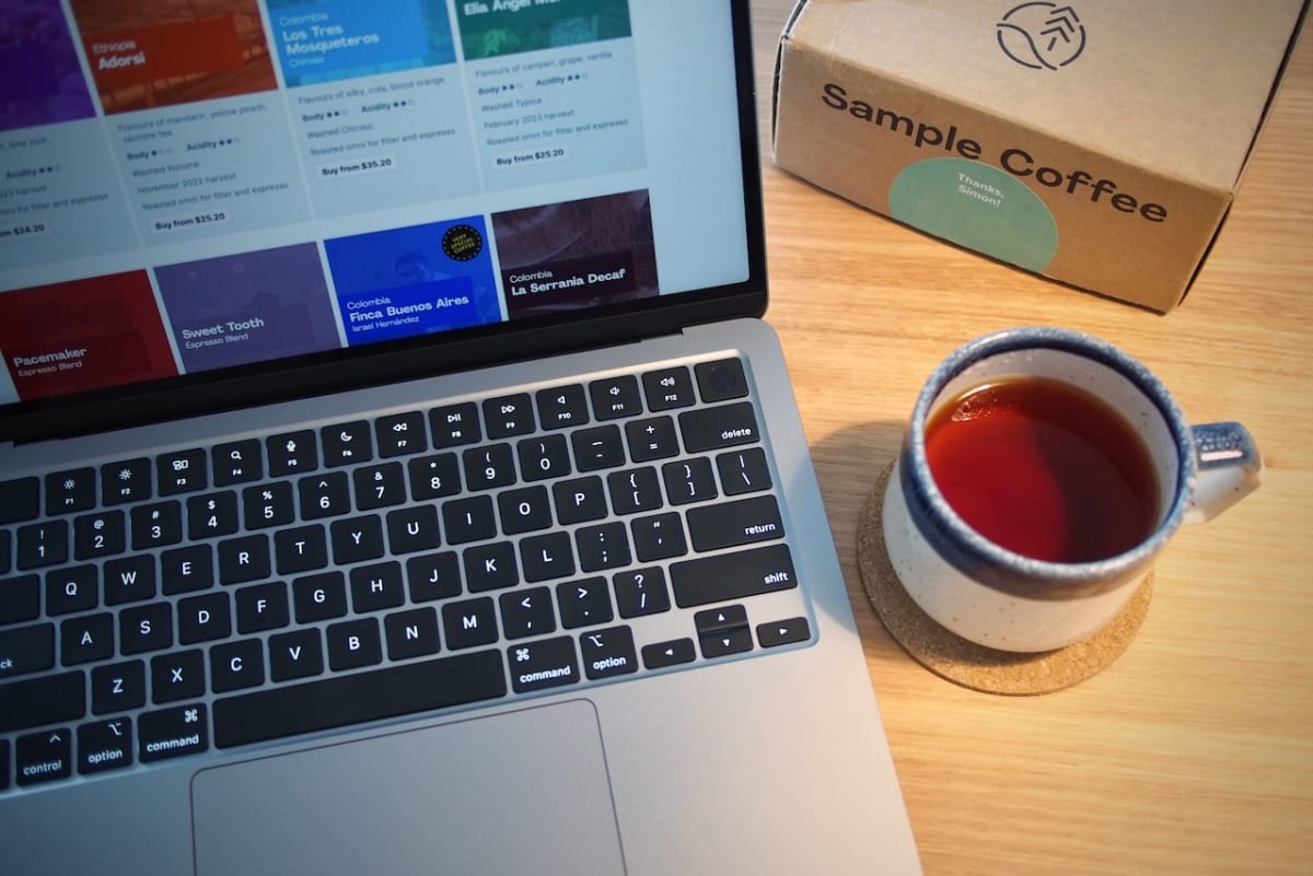 Laptop showing Sample Coffee website, sitting on a table next to a speckled ceramic mug with coffee