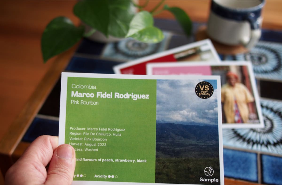 Photo of a hand holding a new postcard, showcasing the Pink Bourbon coffee from Marco Fidel Rodriguez